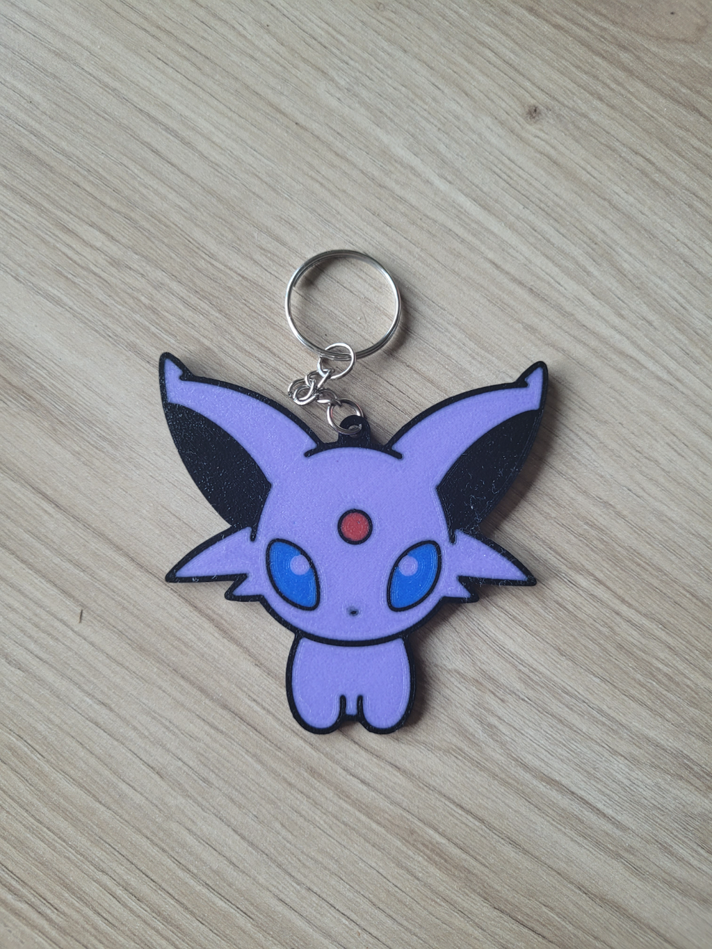 Keychain with a purple cartoon character on a wooden surface Eevee Evolutions. Espeon