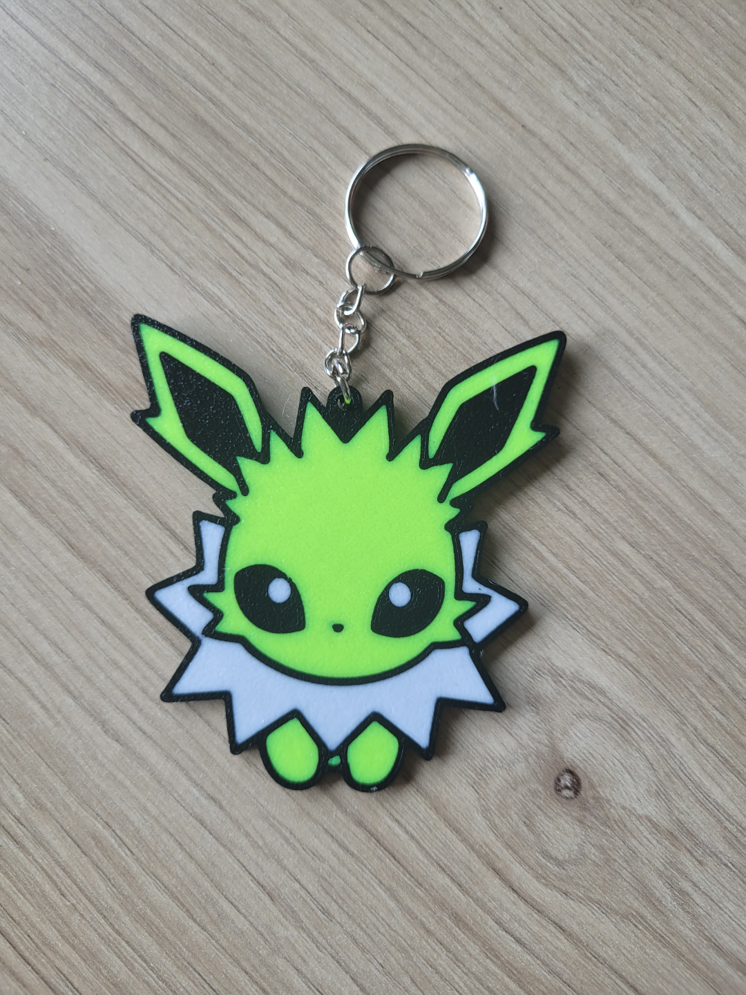 Keychain with a green and black character design on a wooden Eevee Evolutions. Jolteon surface