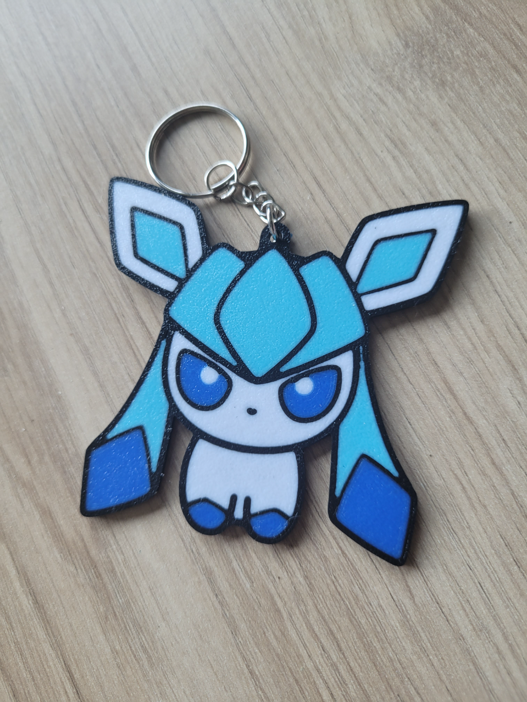 Blue and white cartoon character keychain on a wooden surface Eevee Evolutions. Glaceon
