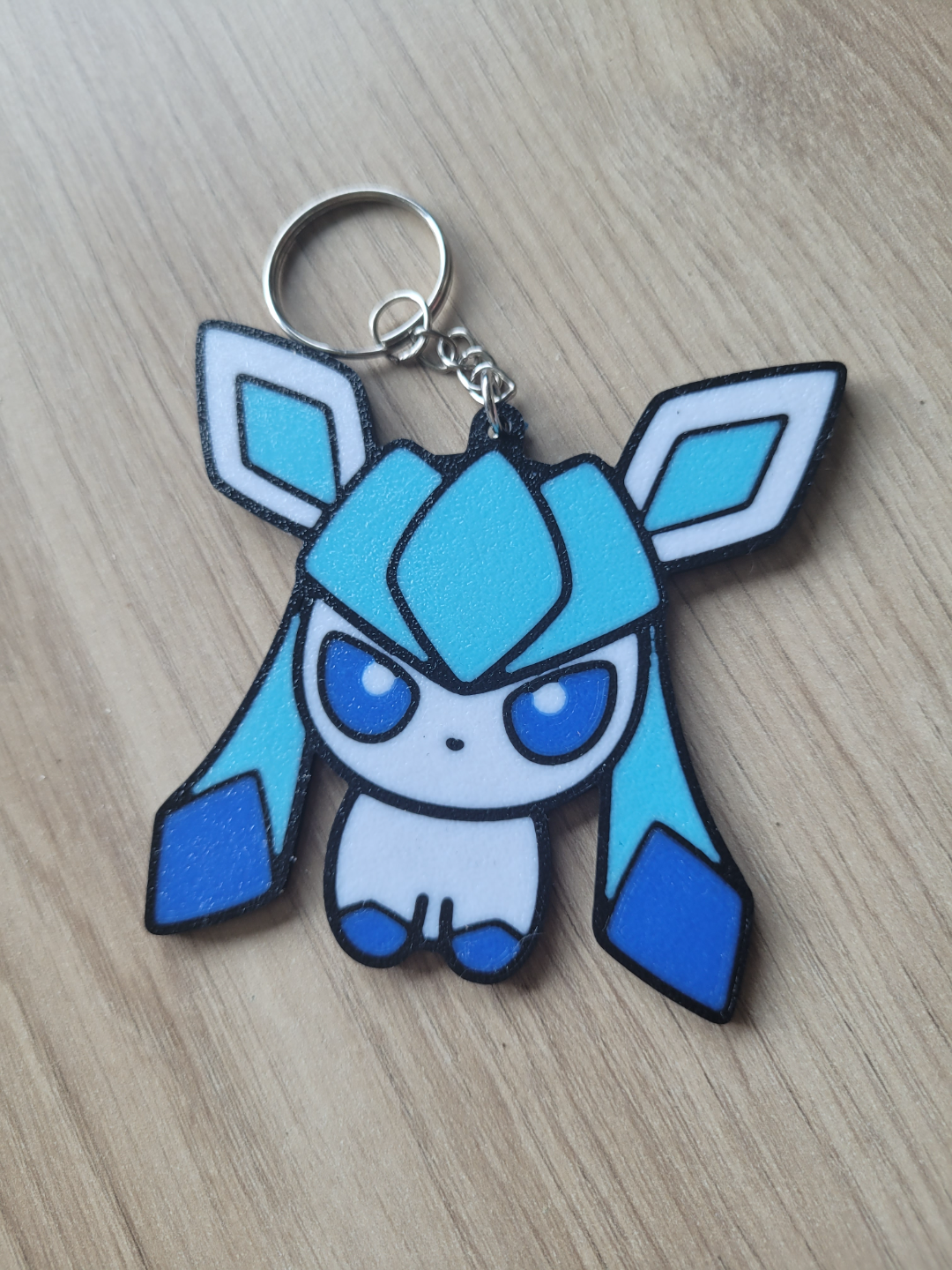 Blue and white cartoon character keychain on a wooden surface Eevee Evolutions. Glaceon