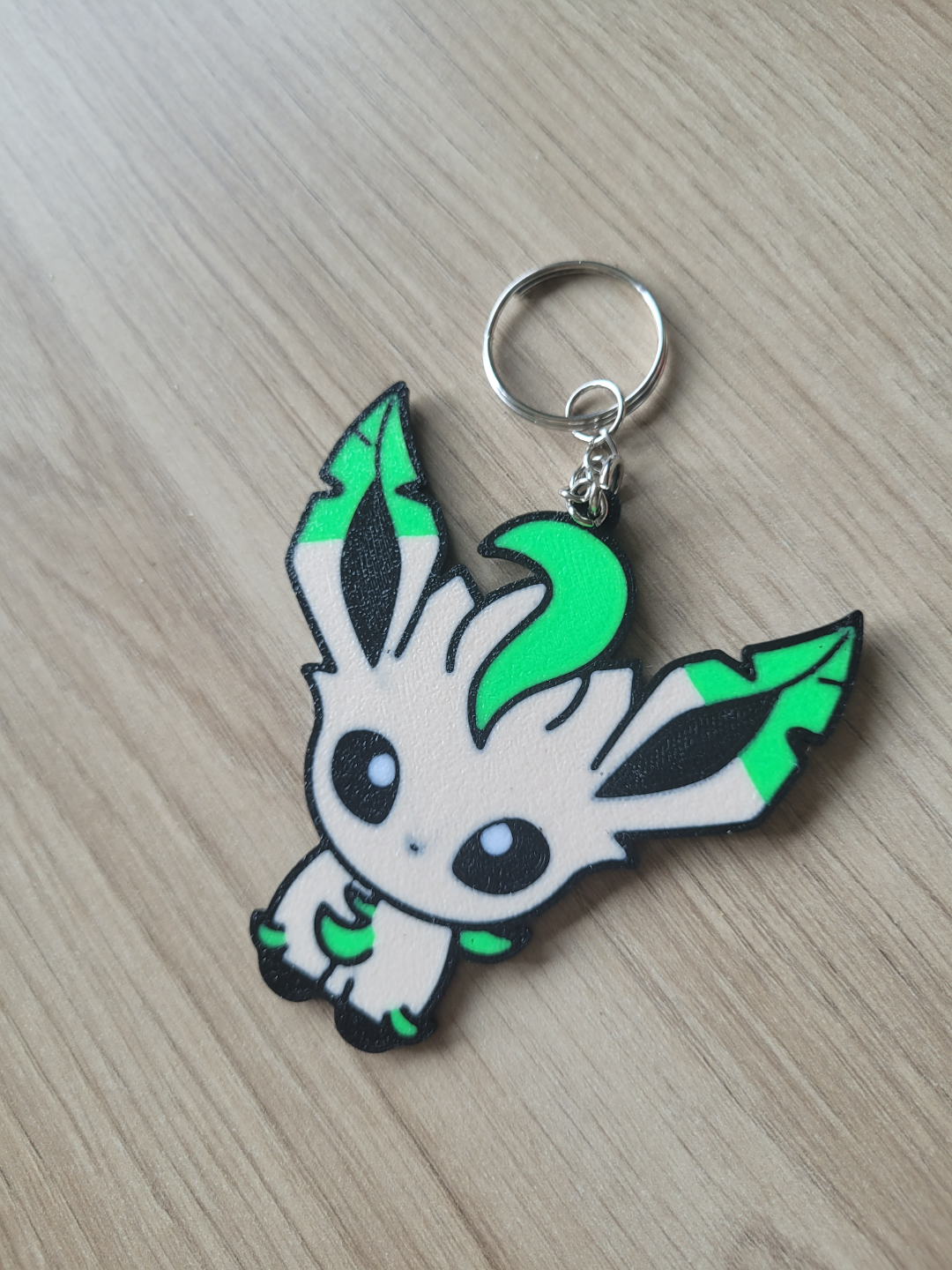 Keychain with a cartoon character design on a wooden surface Eevee Evolutions. Leafeon