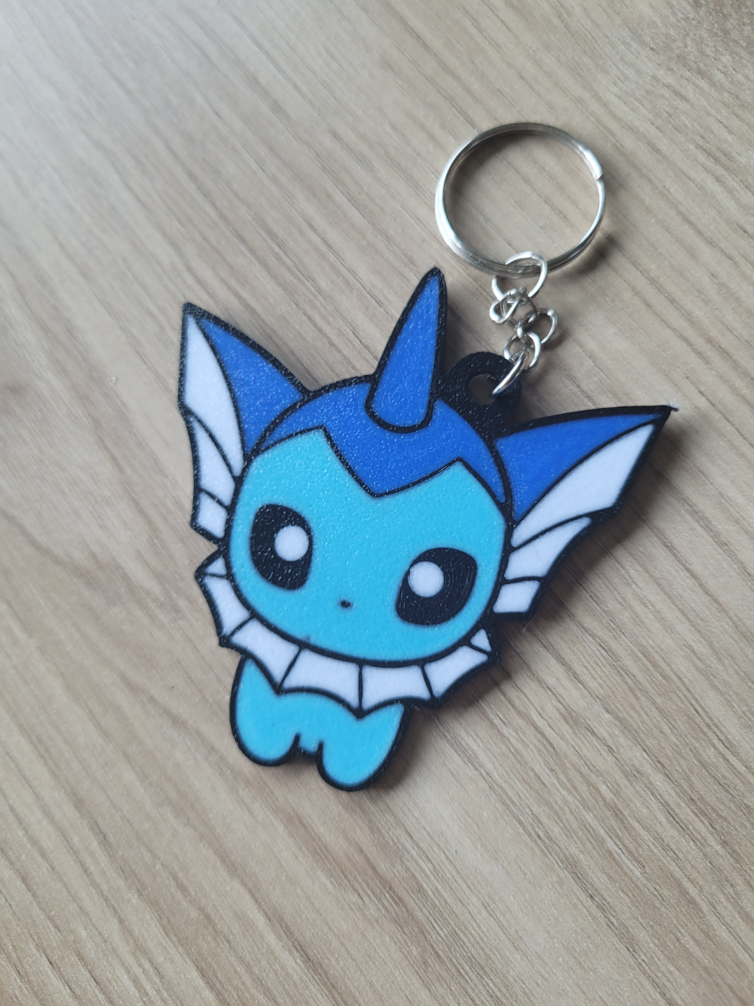 Blue and white cartoon character keychain on a wooden surface Eevee Evolutions. Vaporeon